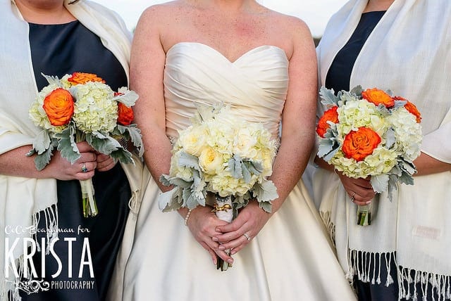 wedding dress code three women smartly dressed in blue and white satijn dresses holding orange bridal bouquets