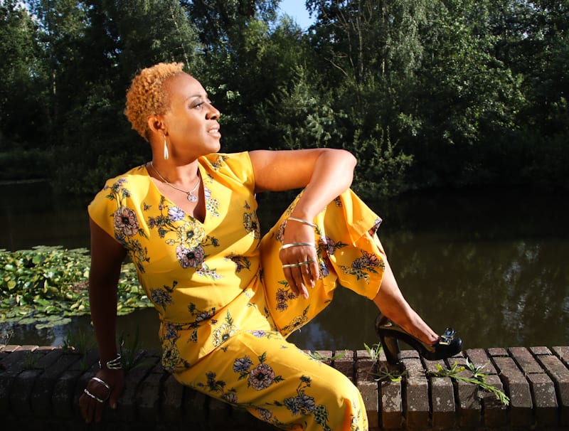 woman of colour with blond hair sitting on a ledge facing the sun