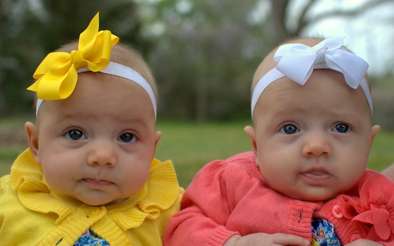 fun naming ceremony two babies dressed in yellow and coral coloured cardigans