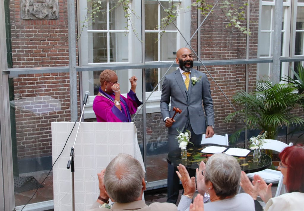 black wedding celebrant Amsterdam native english-speaking woman wearing pink gown and man wearing grey outfit with yellow tie
