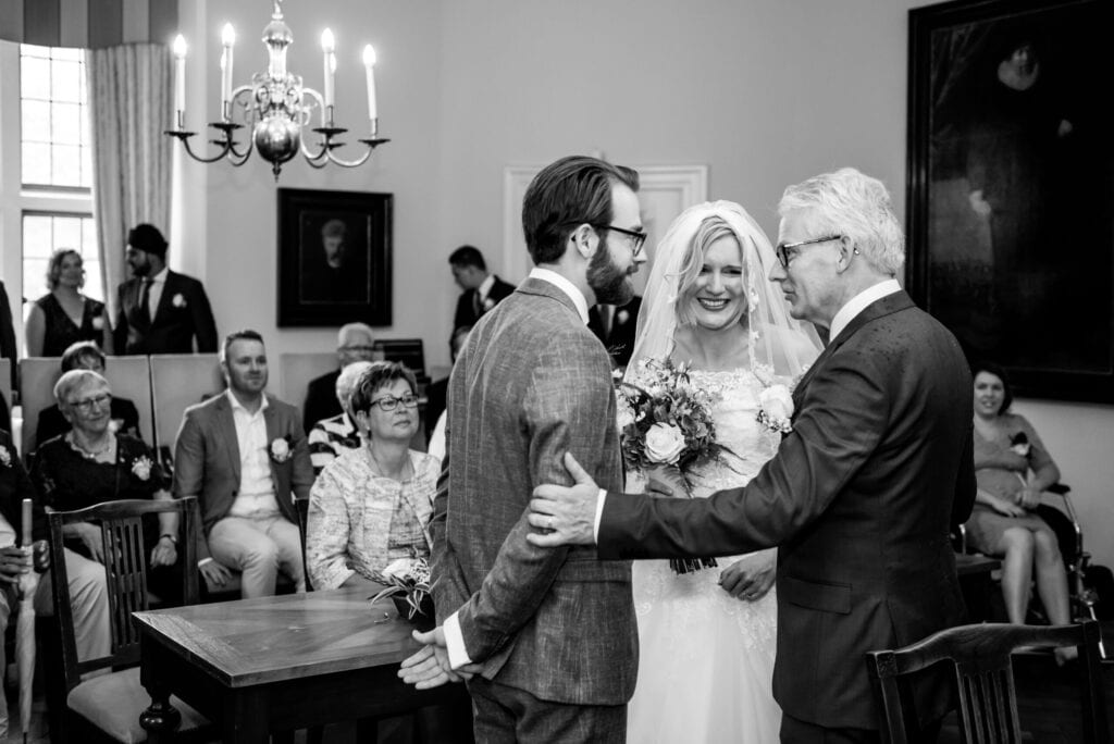 Ceremonieel huwelijk Bruidspaar en vader van de bruid staat achter een trouwtafel en de bruiloftsgasten kijken