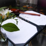 Coronavirus weddings marriage certificate pen and bouquet of white flowers on signing table.