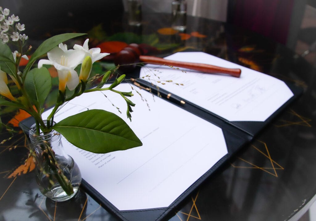Coronavirus weddings marriage certificate pen and bouquet of white flowers on signing table.