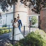 Dutch church weddings bride in white gown and groom in grey suit standing embrace at the gates of the castle