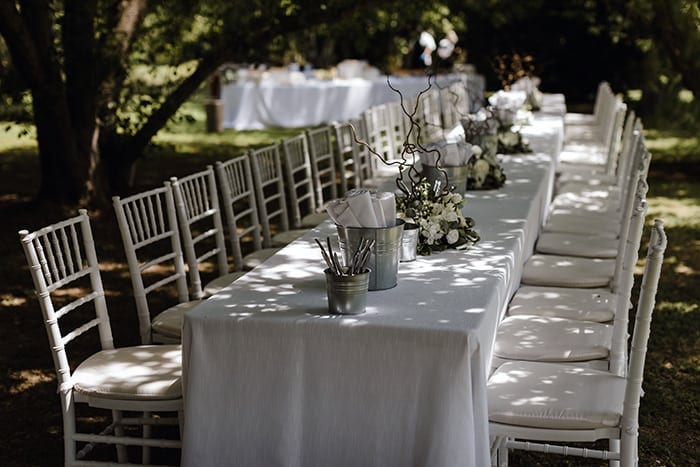 buiten bestek en servetten op een lange tafel met een wit kleed van linen en bloemen als decoratie.