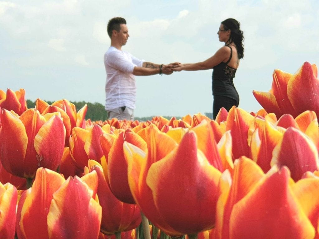 huwelijksrituelen liefdesceremonie afbeelding echtpaar staan hand in hand in een oranje tulipvelden