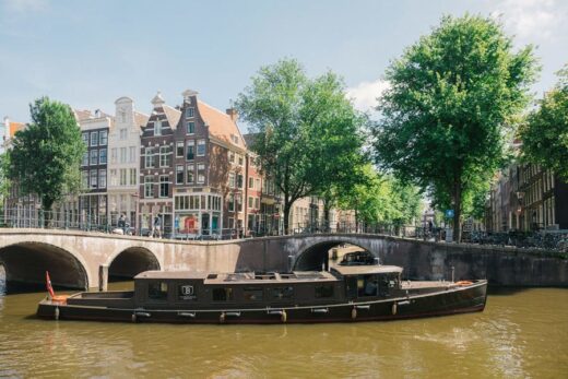 A large ship on the Amsterdam canals with a backdrop of gabled houses.