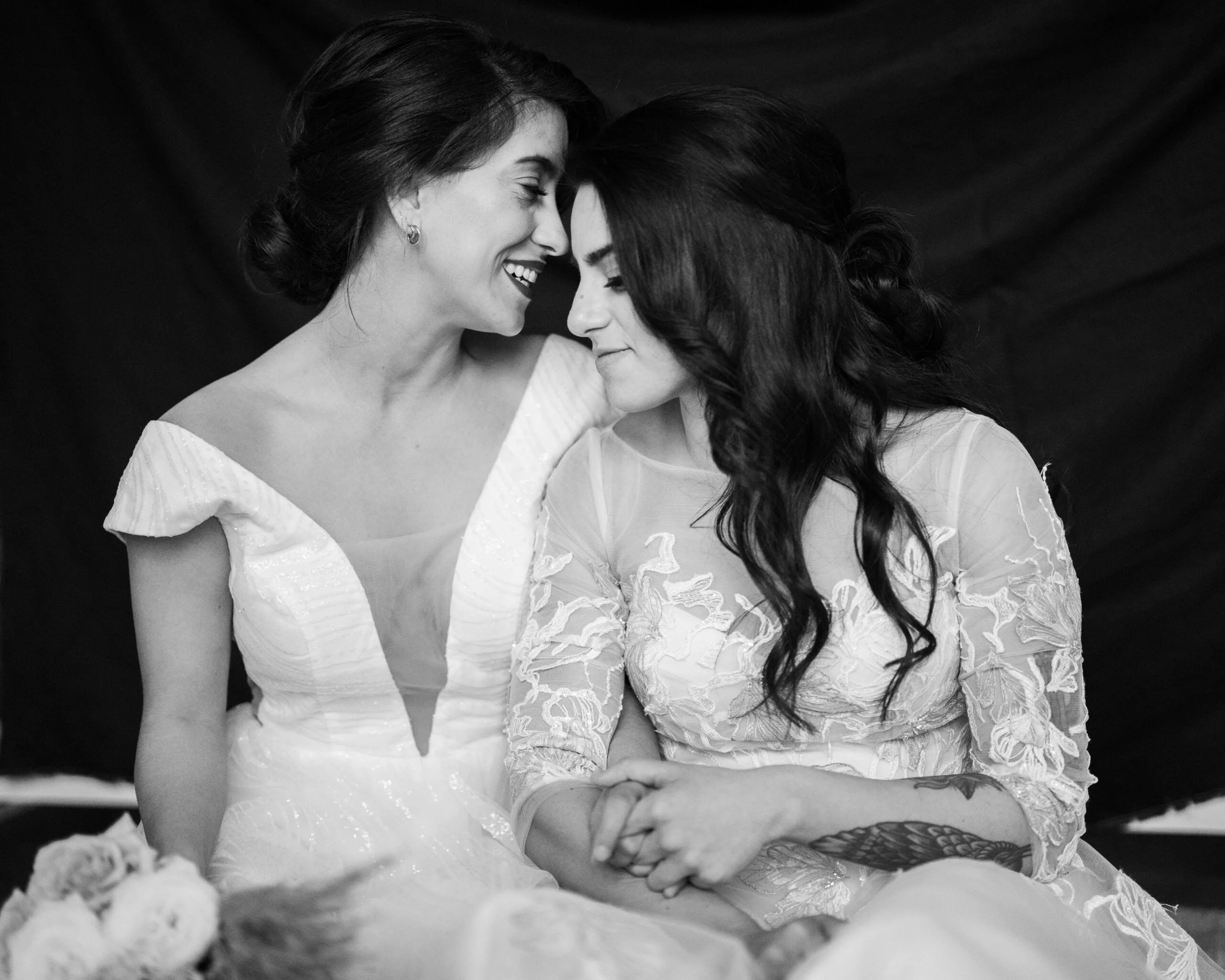 Two happy lesbian LGBT brides kissing on their wedding day. Dressed in beautiful laced bridal dresses embracing, smiling and holding hands.