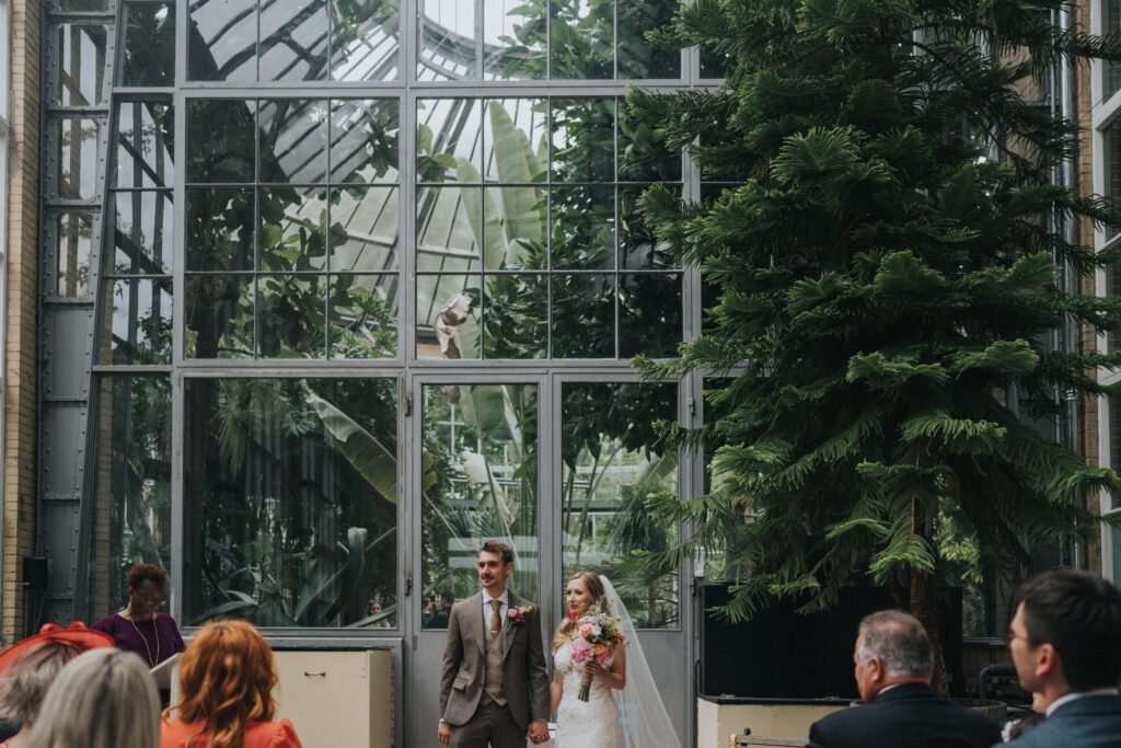 Newlywed Game Interview Questions, marriage officiant with bride and groom holding hands during a ceremony in Hortus Botanicus, Amsterdam
