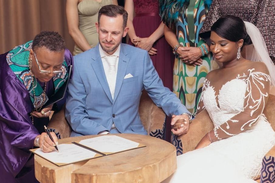 Black tie wedding dress code at Van der Valk Hotel, Almere with officiant signing the certificate, and the bride and groom smiling holding hands. 