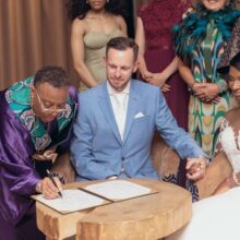 review: bilingual wedding in Amsterdam, officiant signing symbolic certificate and bride and groom as bride and groom look on. tweetalige bruiloft