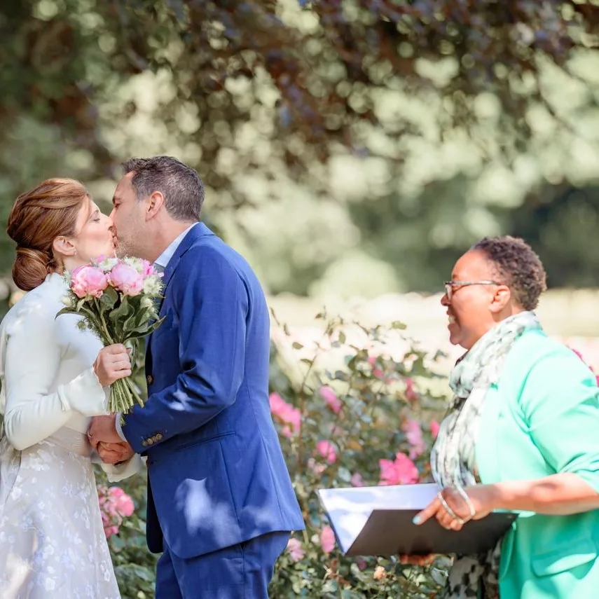 trouwen in het voorjaar unieke bruiloft trends van een ervaren en energieke trouwambtenaar: bruid die een kus krijgt van de bruidegom tijdens een ceremonieel huwelijk in de park