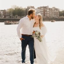 reviews: man with beard wearing white shirt and jeans kissing woman with long blond hair wearing white bridal dress during a canalside wedding ceremony in Amsterdam. 