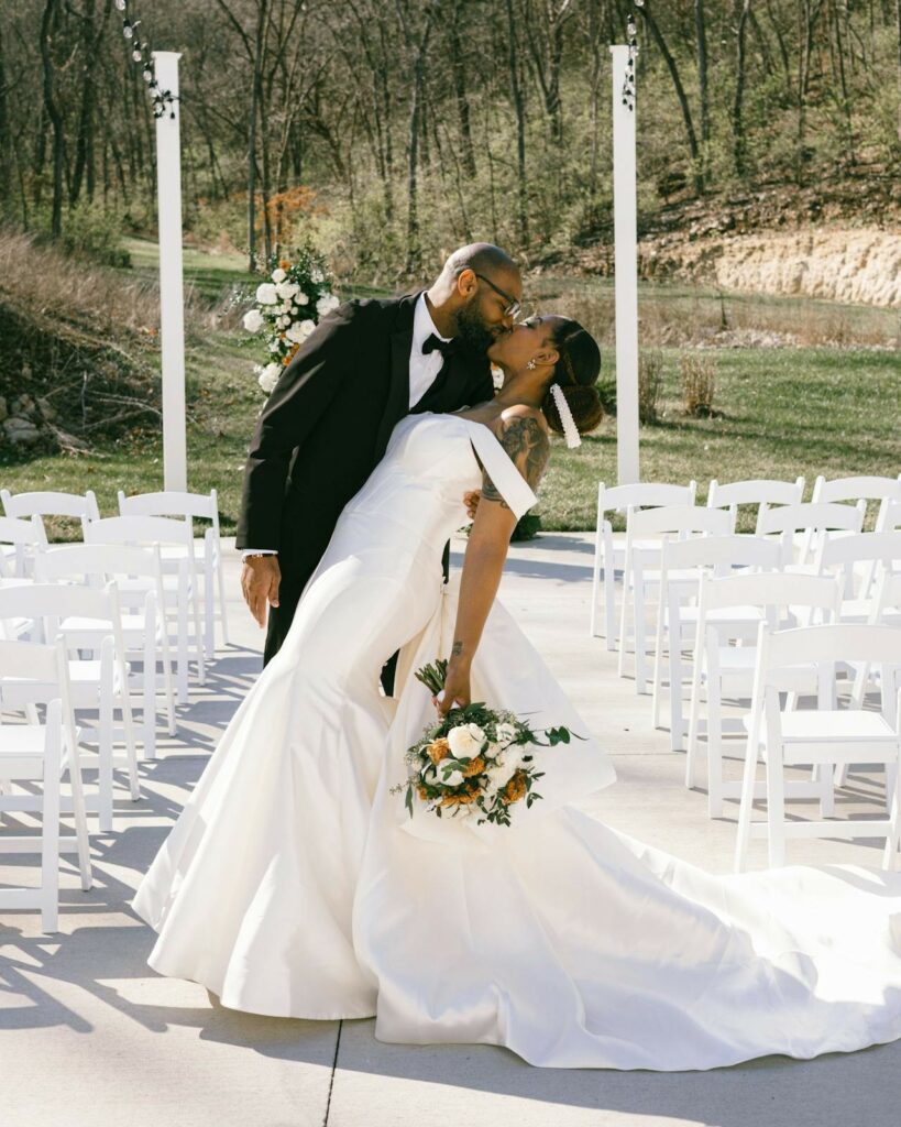 woman in white satin bridal dress and man dressed in white black tuxedo kissing.
