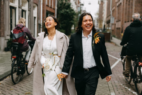 Elopement wedding in Amsterdam with a man and woman holding hands and laughing while walking in the city.